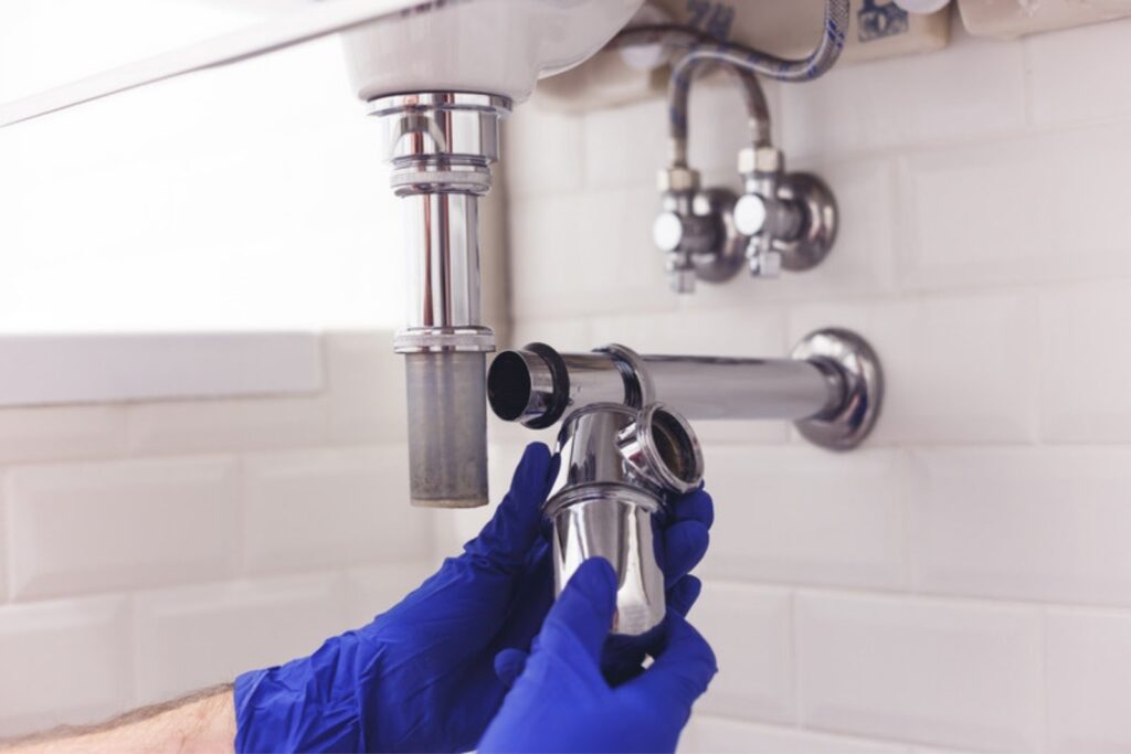 Plumber in blue gloves fitting a chrome sink drain trap